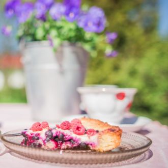 An outdoor table is set with two plates of berry pie and two coffee cups.