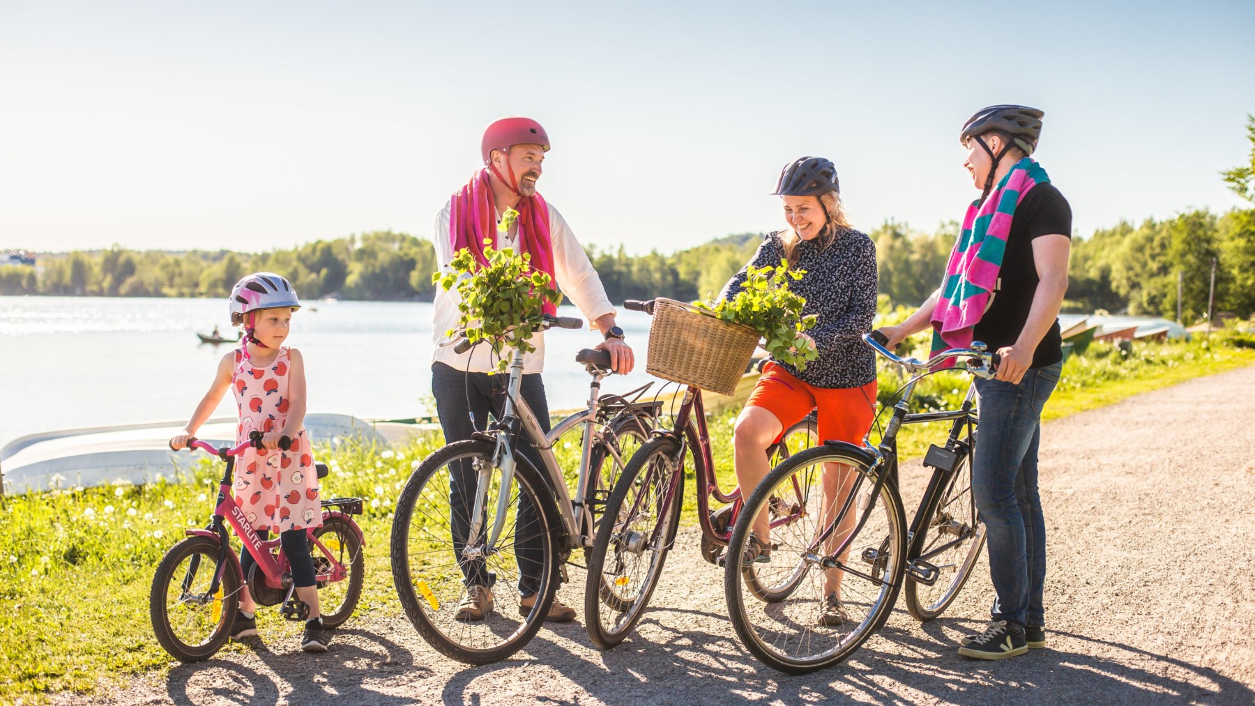 Three adults and one child stand by their bicycles with greenery and a lake in the background.