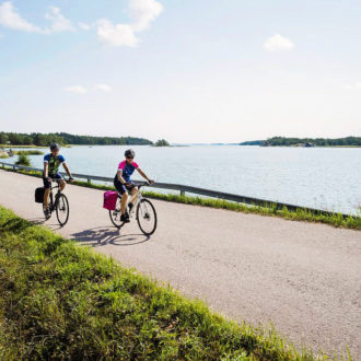 Deux personnes en tenues de sport se promènent à vélo le long d’un sentier côtier en été.