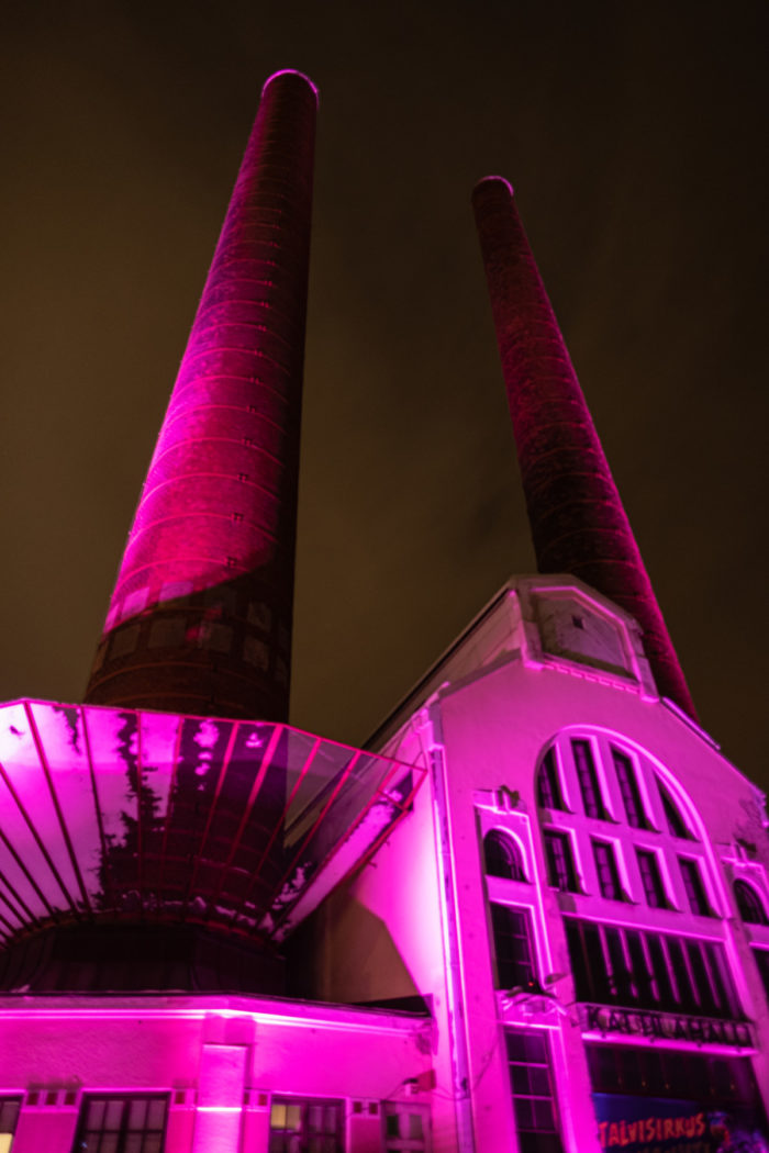 Un edificio y sus dos chimeneas se iluminan con luz rosa.