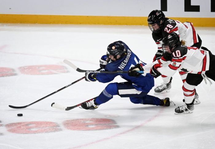 A Finnish hockey player moves past two Canadian players.