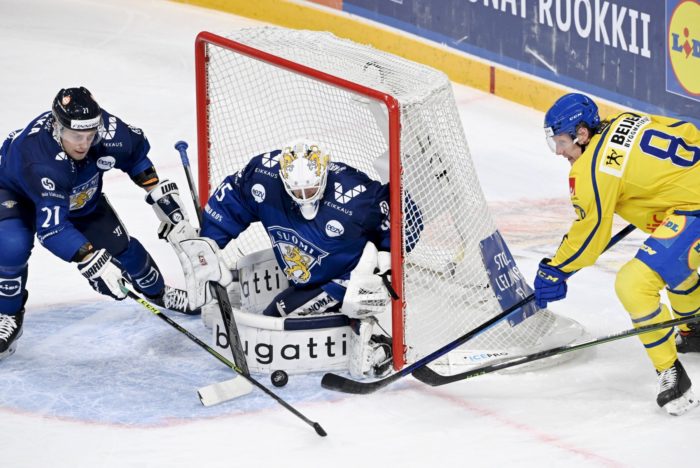 The Finnish goaltender blocks a Swedish player from putting the puck in the net.