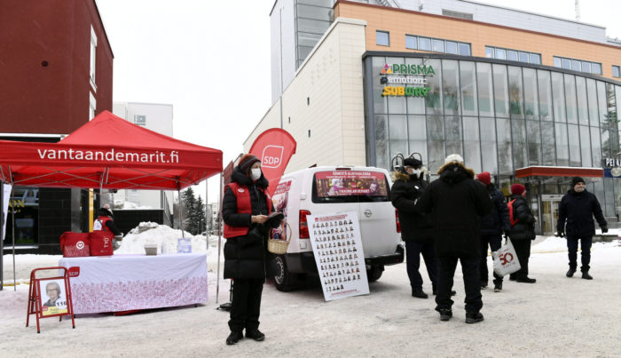 On snow-covered ground in front of a shopping centre, political campaign workers talk with passers-by.