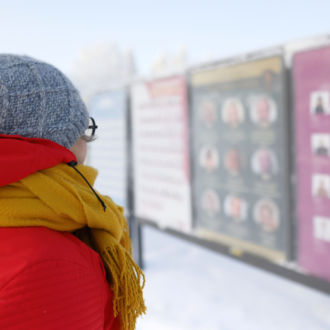 Uma mulher com roupas de inverno olha para uma fileira de cartazes eleitorais.