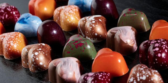 Ряды шоколадных конфет разного цвета в форме сердца.