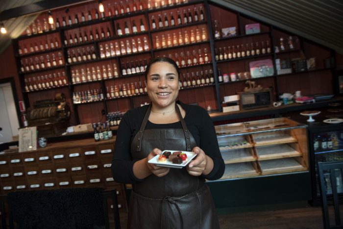 Uma mulher está em frente ao balcão de uma loja, segurando um prato cheio de chocolates.