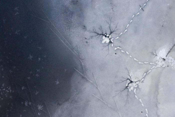 Une vue plongeante révèle des traces de skis et de pas humains dans la neige ainsi que sur une surface d’eau gelée.