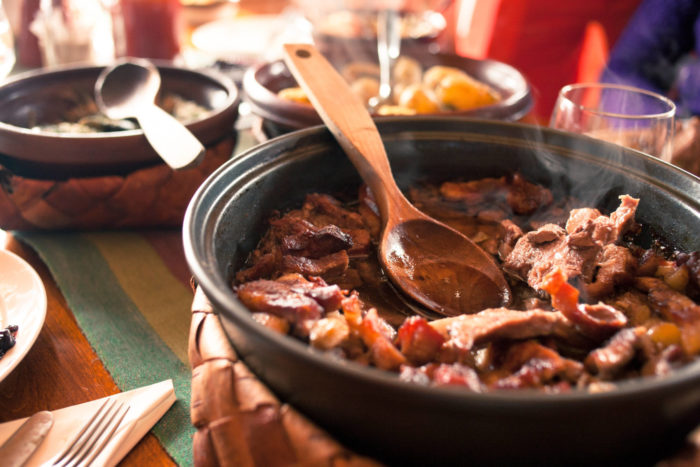 A steaming bowl of meat and vegetables is on a dinner table.