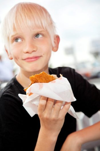 Ein Junge im T-Shirt hält etwas zu essen in einer kleinen Tüte.