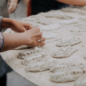 A pair of hands is shaping dough into small pies on a table.