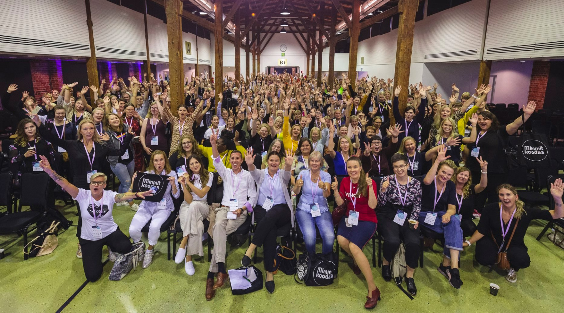 Algumas centenas de pessoas, quase todas mulheres, posam para uma foto de grupo em um salão em um evento de oficina.