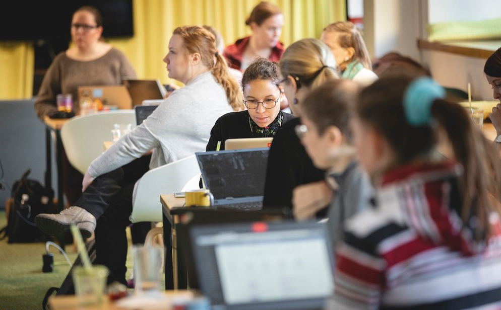 Des femmes de tous âges sont assises dans une salle de classe, faisant face à leurs écrans d’ordinateur.