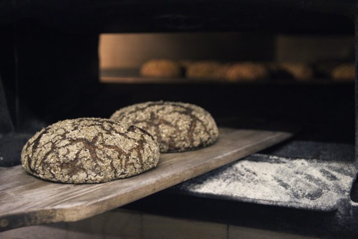 رغيفان من الخبز طازجان مستديران يتم تبرديهما أعلى لوحة خشبية.