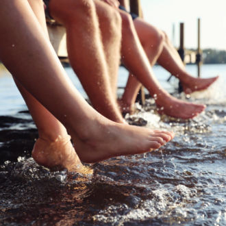 Several people sit on the edge of a dock, kicking their feet in the water.