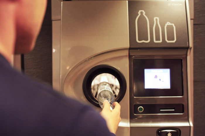 A person feeds a plastic bottle into the opening of a bottle-return machine.