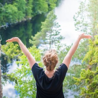 A woman stretches out her arms towards a forest and lake.