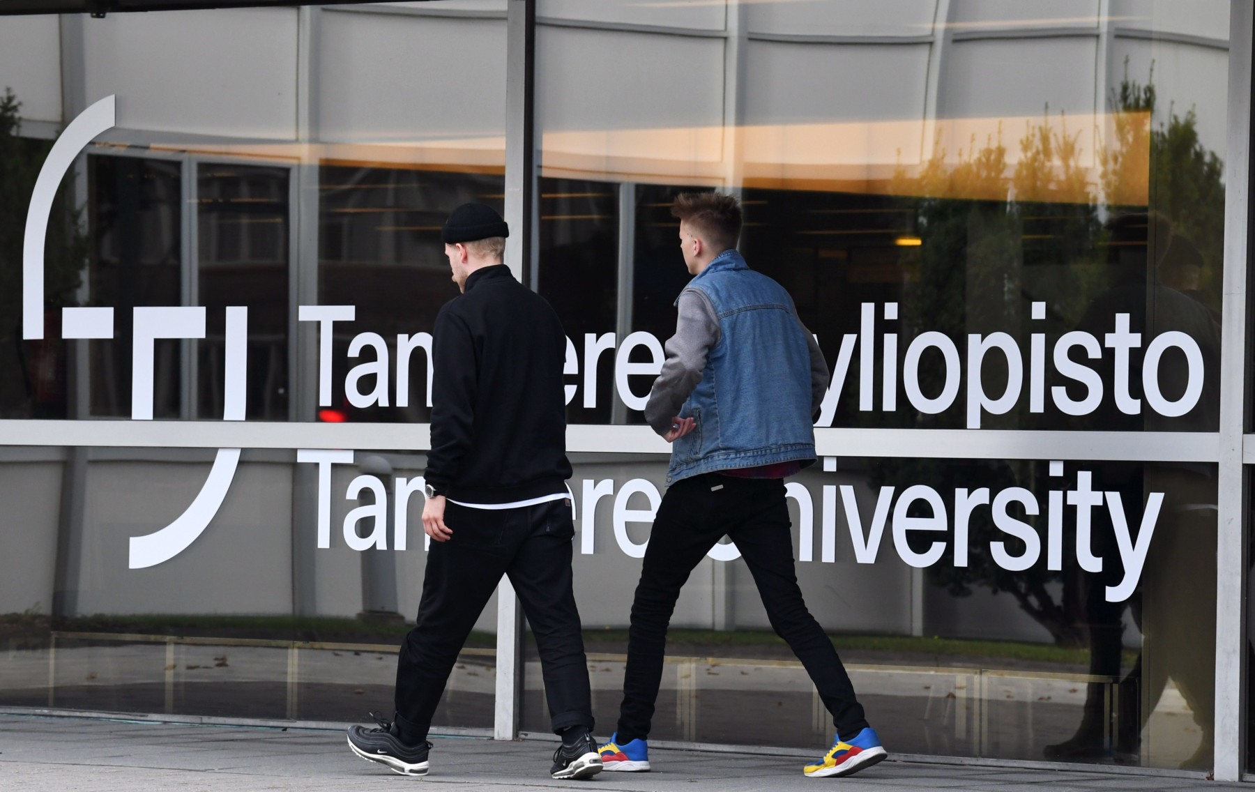 Dos jóvenes pasan junto a un cartel de la Universidad de Tampere.