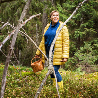 Una mujer que lleva una cesta en la mano posa sonriente en un bosque otoñal.