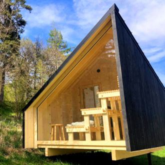 Ein kleines Holzhaus auf einer Seite mit einer gläsernen Wand, durch die Holzbänke sichtbar sind.