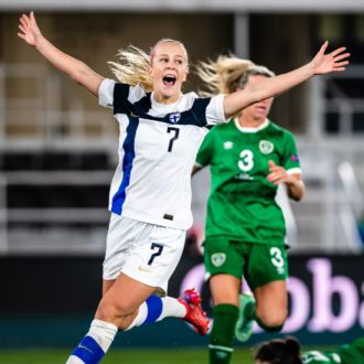 Two Finnish soccer players raise their hands in the air in triumph.