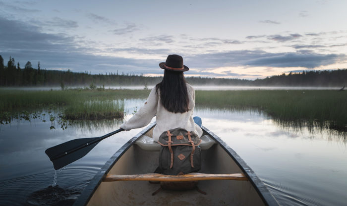 A woman paddles a canoe on a peaceful lake.