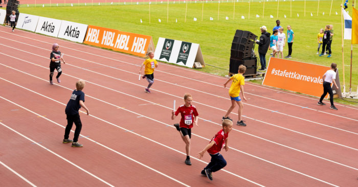 En una pista de atletismo, varios niños de distintos equipos se pasan el testigo en una carrera de relevos.