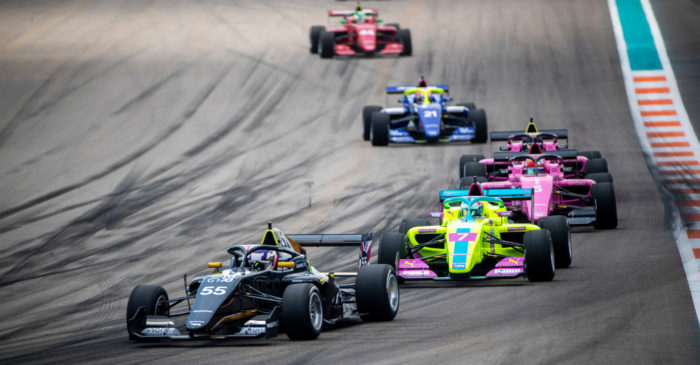 Five racecars drive into a curve on a racetrack.