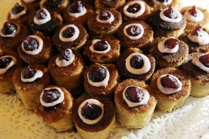 Many rows of small cylindrical cakes topped with frosting and jam are arranged on a table.