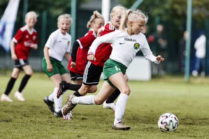 Uma garota ultrapassa várias outras garotas enquanto dribla uma bola de futebol.