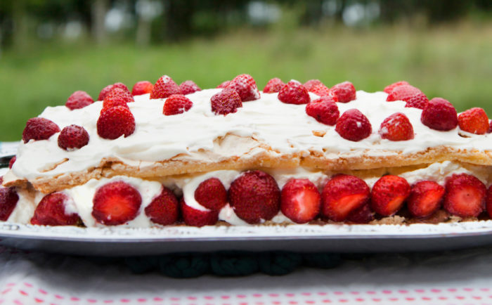 A cake topped with whipped cream and strawberries is on a plate on an outdoor table.