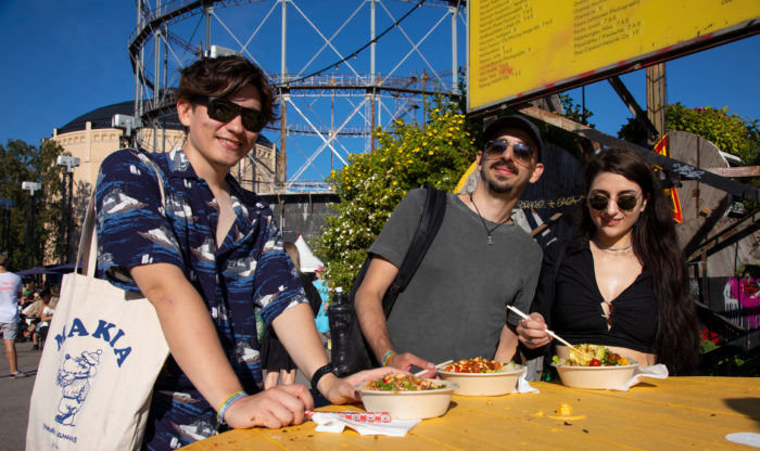 Deux hommes et une femme portant des lunettes de soleil sont en train de déjeuner à une table installée en plein air.