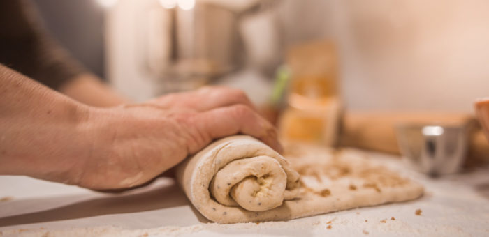 Deux mains sont en train de rouler une feuille de pâte à gâteau épaisse sur une table.