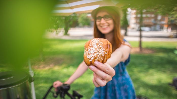 A woman is holding out a cinnamon bun so that it is close to the camera.