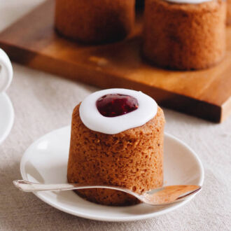 A small cake sits on a plate beside a cup of coffee.