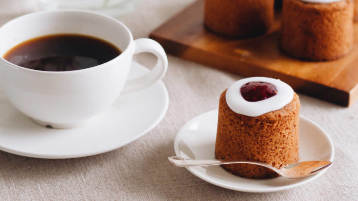 A small cake sits on a plate beside a cup of coffee.