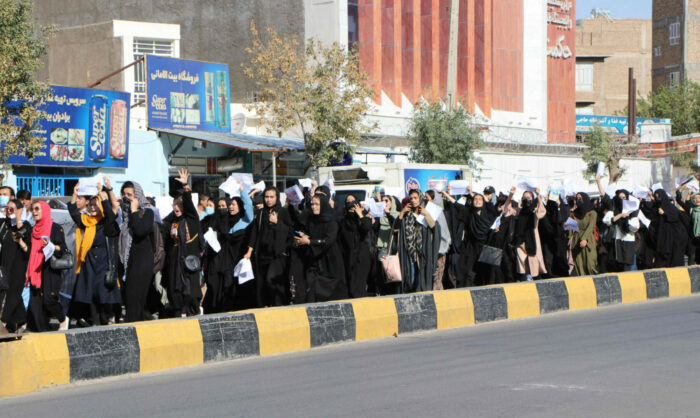 A large group of women, mainly dressed in black, march along a road in a demonstration.