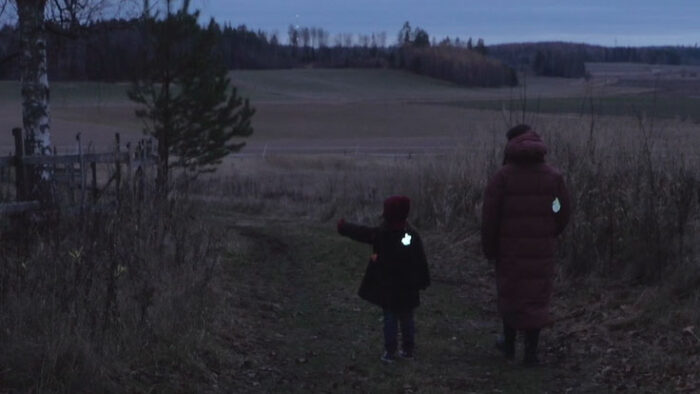 Взрослый и ребёнок идут по дороге по полю. На спинах курток у обоих есть светоотражатели.