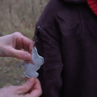 Руки прикрепляют рефлектор в виде муми-тролля к пальто ребёнка.