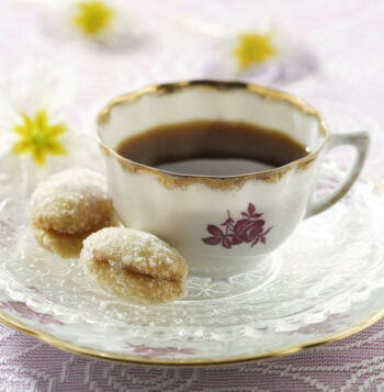 Deux biscuits enrobés de sucre en poudre sont posés sur une soucoupe à côté d’une tasse de café. 