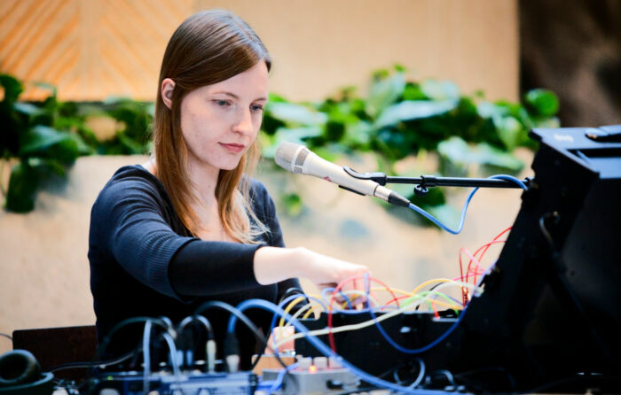 A woman tinkers with a sound system that includes a microphone and an audio mixing board.