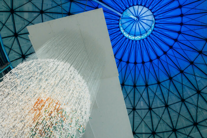 Une vaste coupole en verre est illuminée en bleu tandis que des rangées de perles blanches pendent sous la verrière.