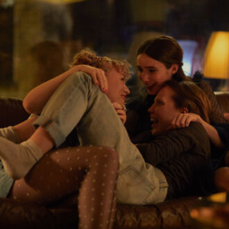 Three women are laughing together on a sofa.