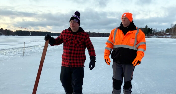 Two men dressed in heavy winter clothing walk on a frozen lake surface.