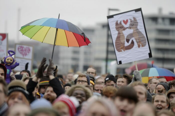 A crowd of people carry signs and rainbow-coloured umbrellas.