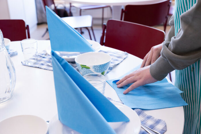 On voit deux mains plier des serviettes sur une table. 