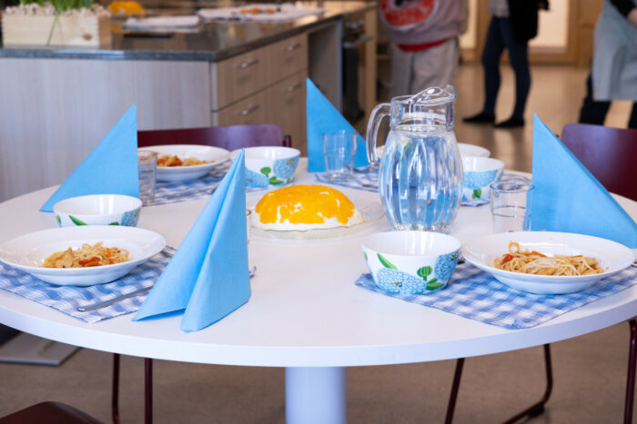 Quatre assiettes remplies de nourriture encadrées de leurs couverts sont disposées sur une table circulaire.