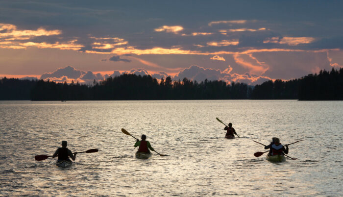 Four kayaks make their way across a lake in the dusky light of evening.
