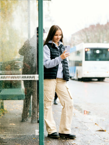 A pre-teen girl stands at a bus stop, looking at her mobile phone.