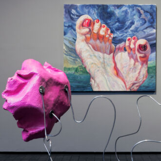 In the background is a painting, a close-up view of two feet with water, greenery and clouds visible behind them, while the foreground contains a sculpture that looks like giant pink flowery shapes on metal stems, with video screens inside the flowers.