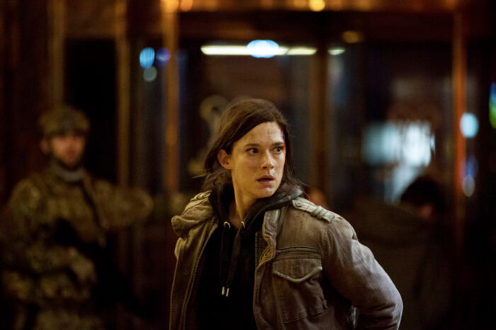 Una mujer que lleva una chaqueta militar observa con expresión tensa algo que queda fuera del encuadre de la foto.